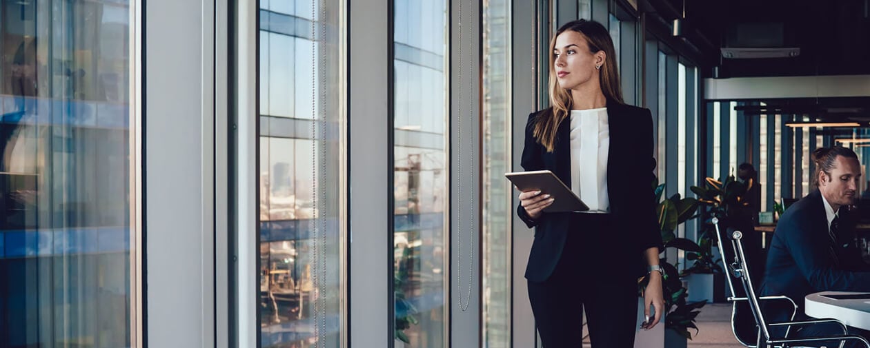 Confident business woman looking at window passing with touchpad