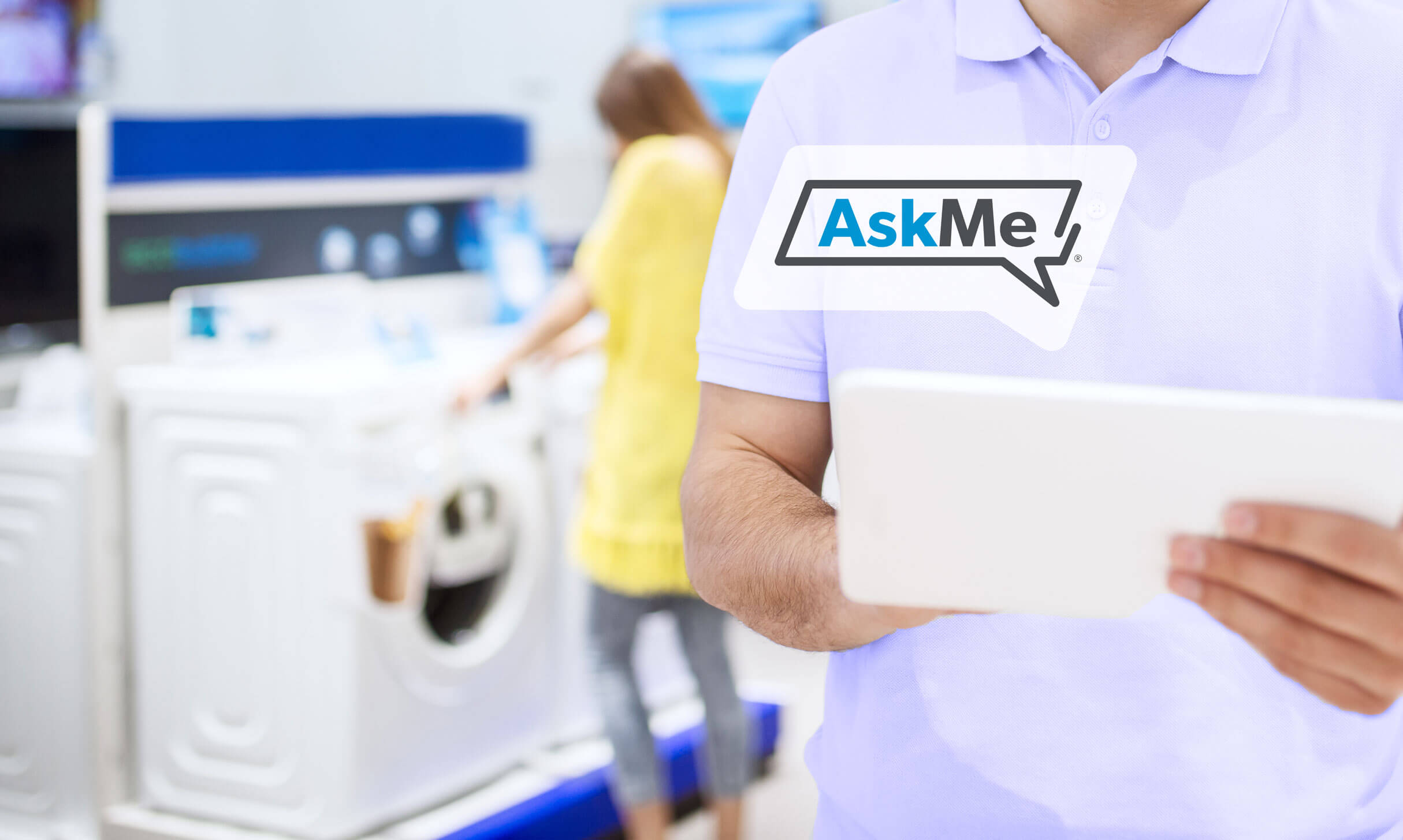 A man in a home appliance retail section receiving virtual help on a tablet while a woman in the background looks at a washing machine