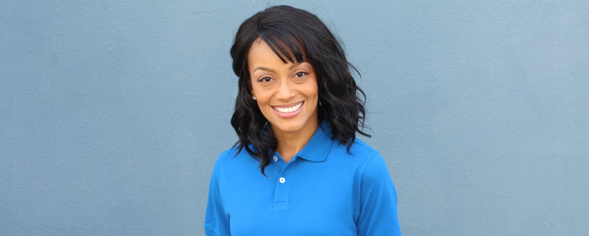 Photo of a retail rep in a blue polo uniform shirt smiling in front of a blue wall
